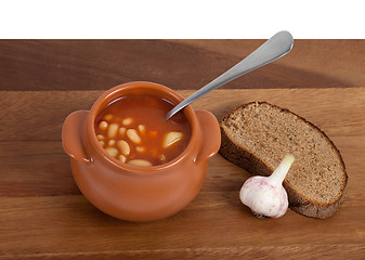 Image showing Soup in ceramic pot with bread and garlic on wooden table
