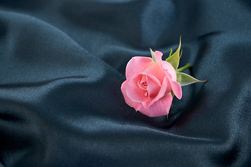 Image showing A pink rosebud lying on blue satin