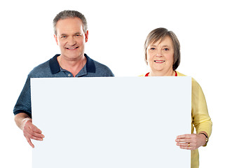 Image showing Smiling aged couple holding blank white poster