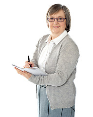 Image showing Aged woman writing on spiral notebook