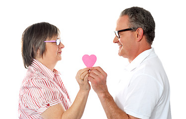 Image showing Aged couple holding paper heart. Smiling at each other