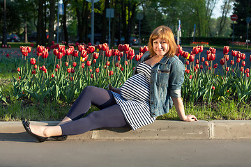 Image showing Pregnant woman sitting near tulip flowerbed