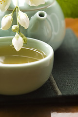 Image showing Green tea with jasmine in cup and teapot on wooden table