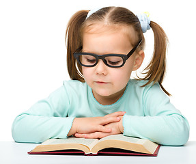 Image showing Little girl reads a book while wearing glasses