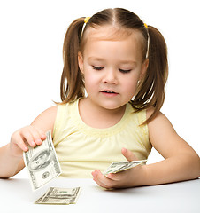 Image showing Cute cheerful little girl is counting dollars