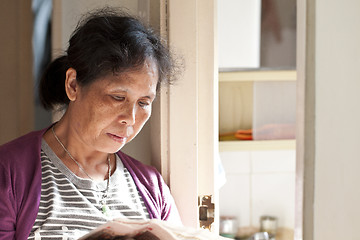 Image showing A 50s asian woman reading newspaper at home