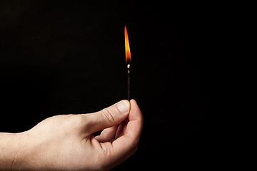 Image showing Hand holding burning match stick on black background