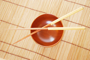 Image showing Chopsticks with wooden bowl on bamboo matting background 