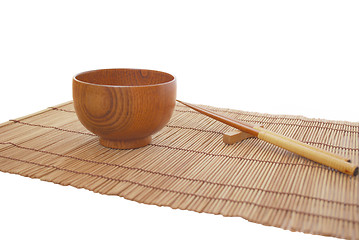Image showing Chopsticks with wooden bowl on bamboo matting background 