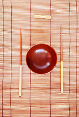 Image showing Chopsticks with wooden bowl on bamboo matting background 