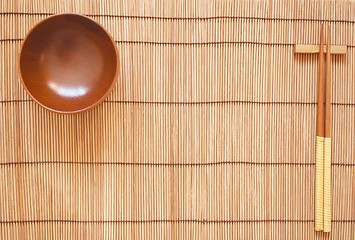 Image showing Chopsticks with wooden bowl on bamboo matting background 