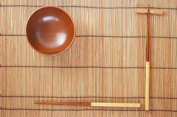 Image showing Chopsticks with wooden bowl on bamboo matting background 