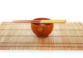 Image showing Chopsticks with wooden bowl on bamboo matting background 