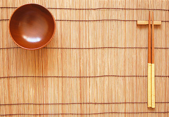 Image showing Chopsticks with wooden bowl on bamboo matting background