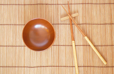 Image showing Chopsticks with wooden bowl on bamboo matting background 