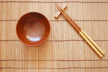 Image showing Chopsticks with wooden bowl on bamboo matting background 
