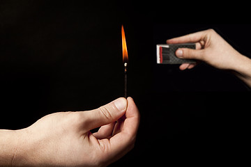 Image showing Hand holding burning match stick on black background