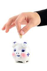 Image showing Hand inserting coin into piggy-bank