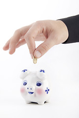 Image showing Hand inserting coin into piggy-bank