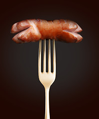 Image showing Grilled sausage on a fork on black background