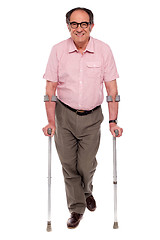 Image showing Smiling senior man walking with two crutches