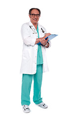 Image showing Aged doctor holding clipboard. Full length shot
