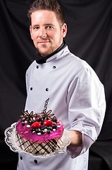 Image showing Handsome confectioner with cake against dark background