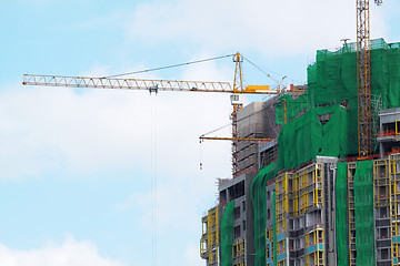 Image showing Building crane and building under construction against blue sky 