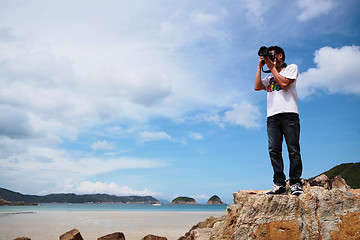 Image showing Portrait of a young man standing on a beach with a camera 