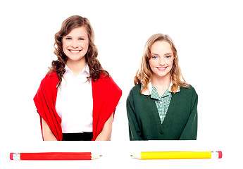 Image showing Big pencils lying in front of two school girls