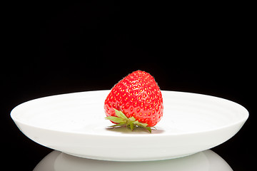 Image showing white saucer with red strawberr on a black background