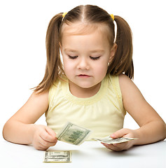 Image showing Cute cheerful little girl is counting dollars