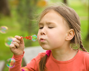 Image showing Cute little girl is blowing soap bubbles