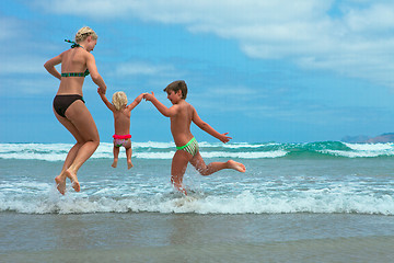 Image showing Mother and two kids  jumping on beach 