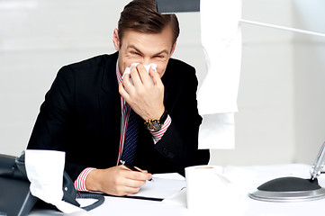 Image showing Professional sitting at desk sneezing into tissue