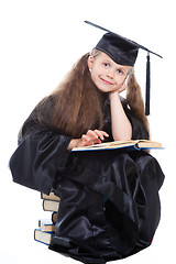 Image showing girl in black academic cap and gown reading big blue book