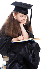Image showing girl in black academic cap and gown reading big blue book