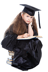 Image showing girl in black academic cap and gown reading big blue book