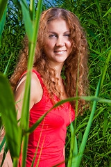 Image showing beautiful girl in red among high green grass of summer meadow