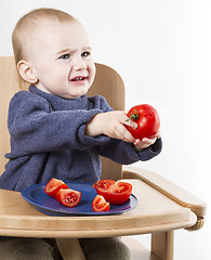 Image showing young child eating tomatoes in high chair