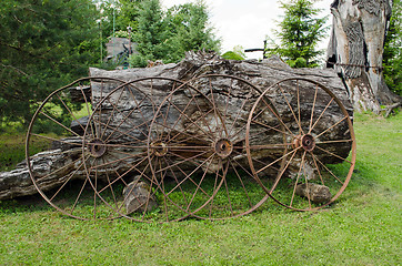 Image showing Old rusty carriage wheels lean to old tree trunk 