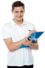 Image showing Smiling young man writing on notepad