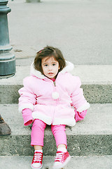 Image showing Little girl in winter clothes sitting in stairs looking at the c