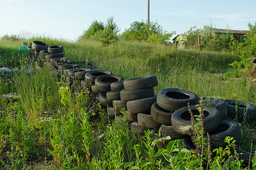 Image showing Fence of old used tires in meadow. Pollution 