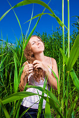 Image showing beautiful girl braiding a plait among high green grass of summer meadow