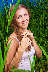 Image showing beautiful girl braiding a plait among high green grass of summer meadow