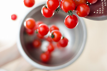 Image showing Cherry Tomatoes Tumbling From Metal Colander Into Metal Pan