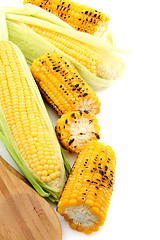 Image showing Cleaning freshly roasted ears of corn on cob with green leaves.