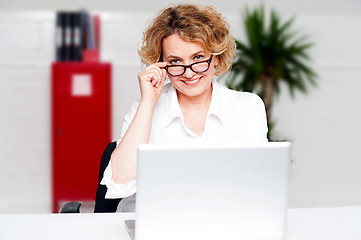 Image showing Aged woman holding glasses working on laptop