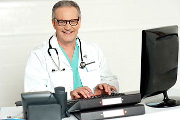 Image showing Aged male doctor in glasses working on computer